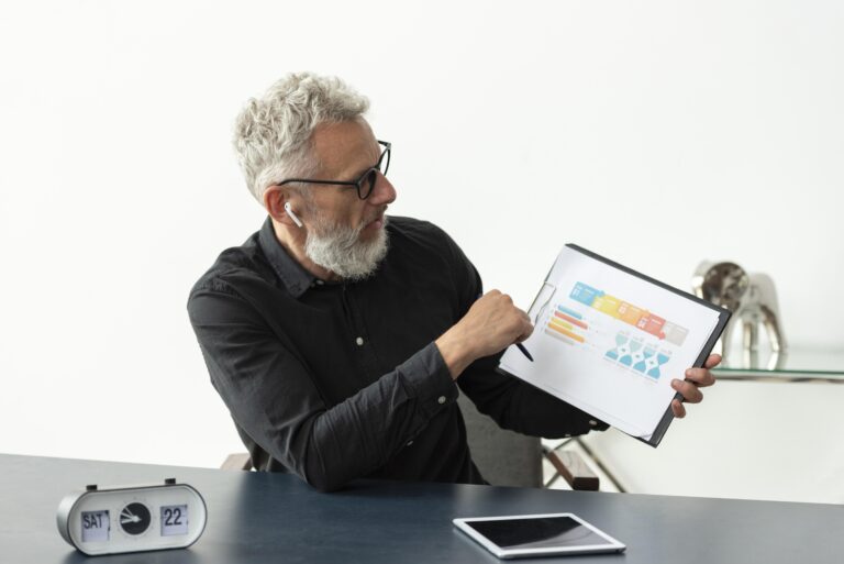 alterer-mann-zu-hause-mit-grafik-auf-notizblock-mit-tablet-auf-dem-schreibtisch.jpg