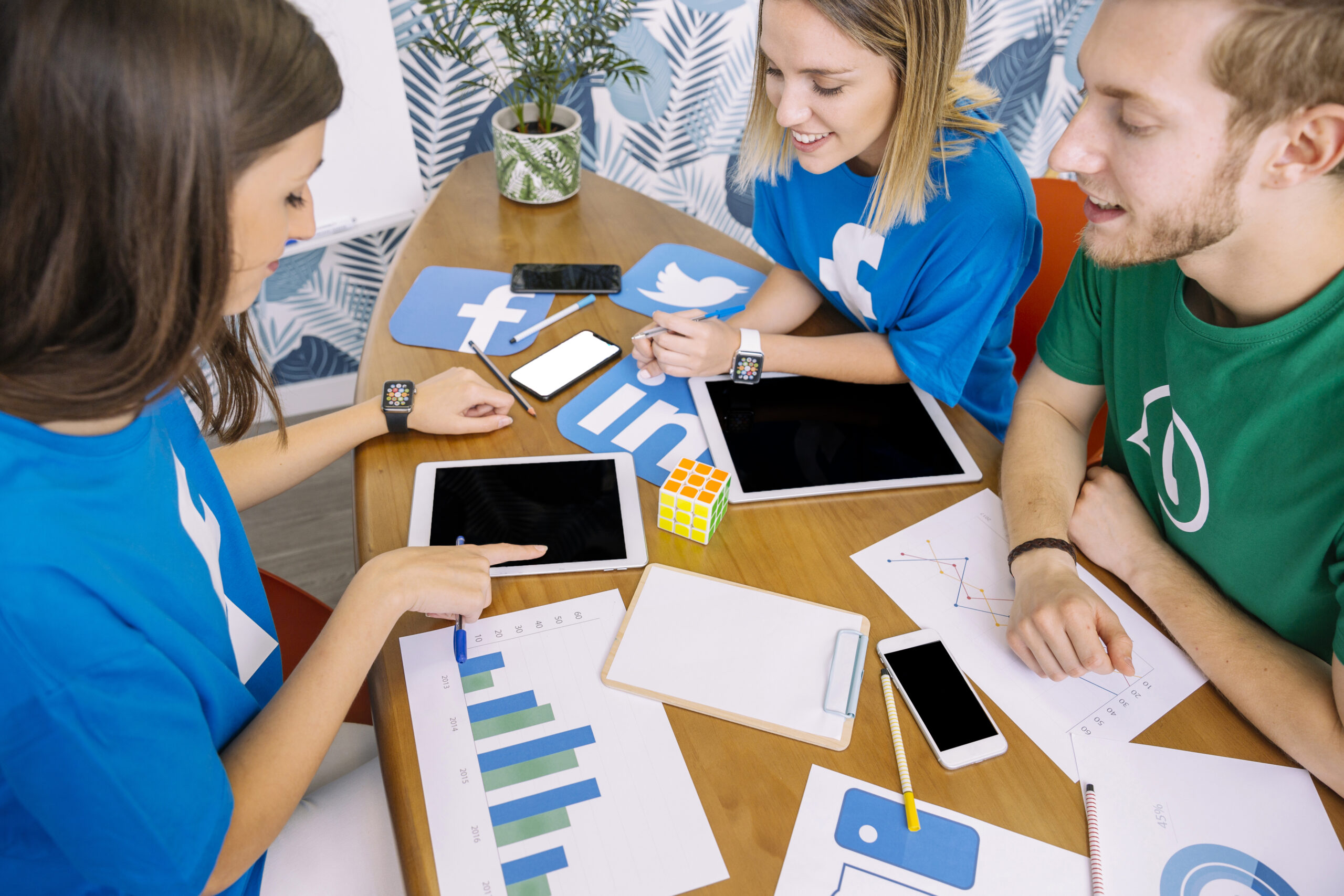 gruppe-von-personen-die-digitale-tablette-mit-social-media-ikonen-am-arbeitsplatz-betrachtet