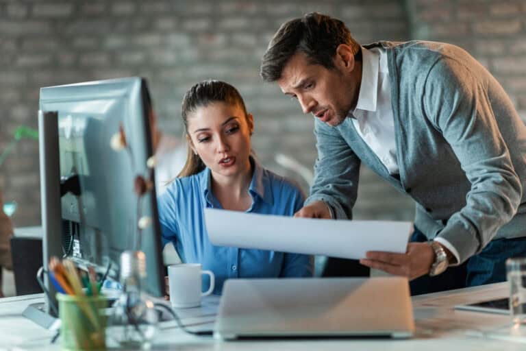 two-business-colleagues-talking-while-working-new-project-examining-blueprints-office-