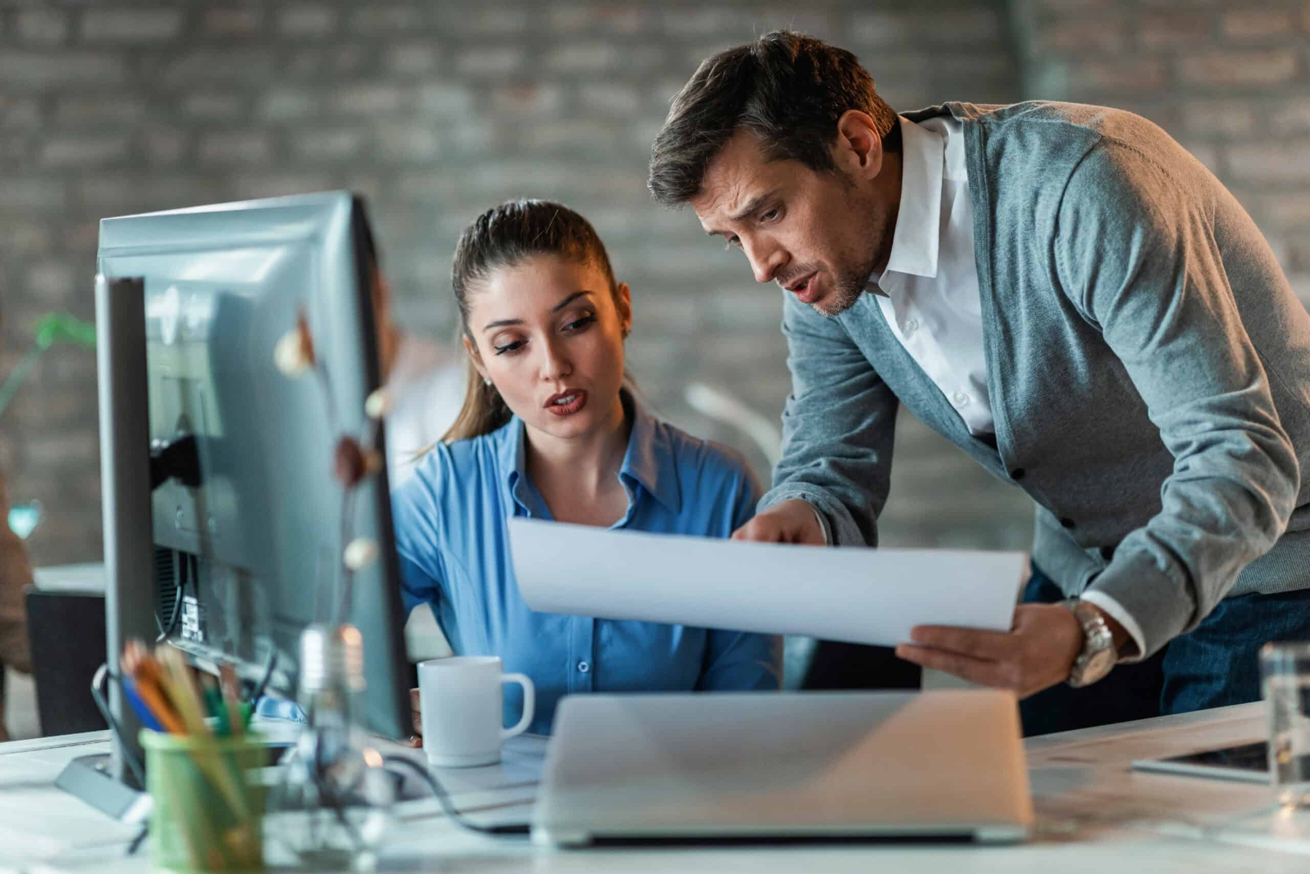 two-business-colleagues-talking-while-working-new-project-examining-blueprints-office-